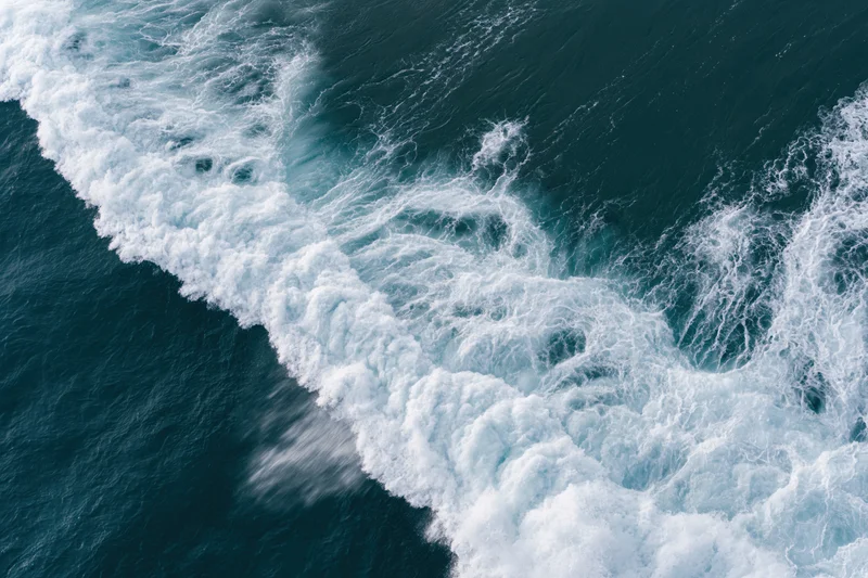 Aerial top-down view of a breaking ocean wave with white foam and churning water