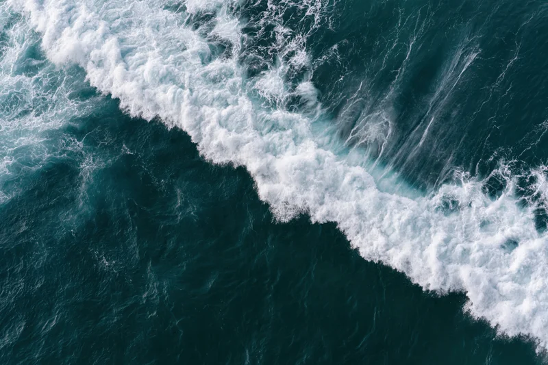 Aerial top-down view of a breaking ocean wave with white foam and churning water