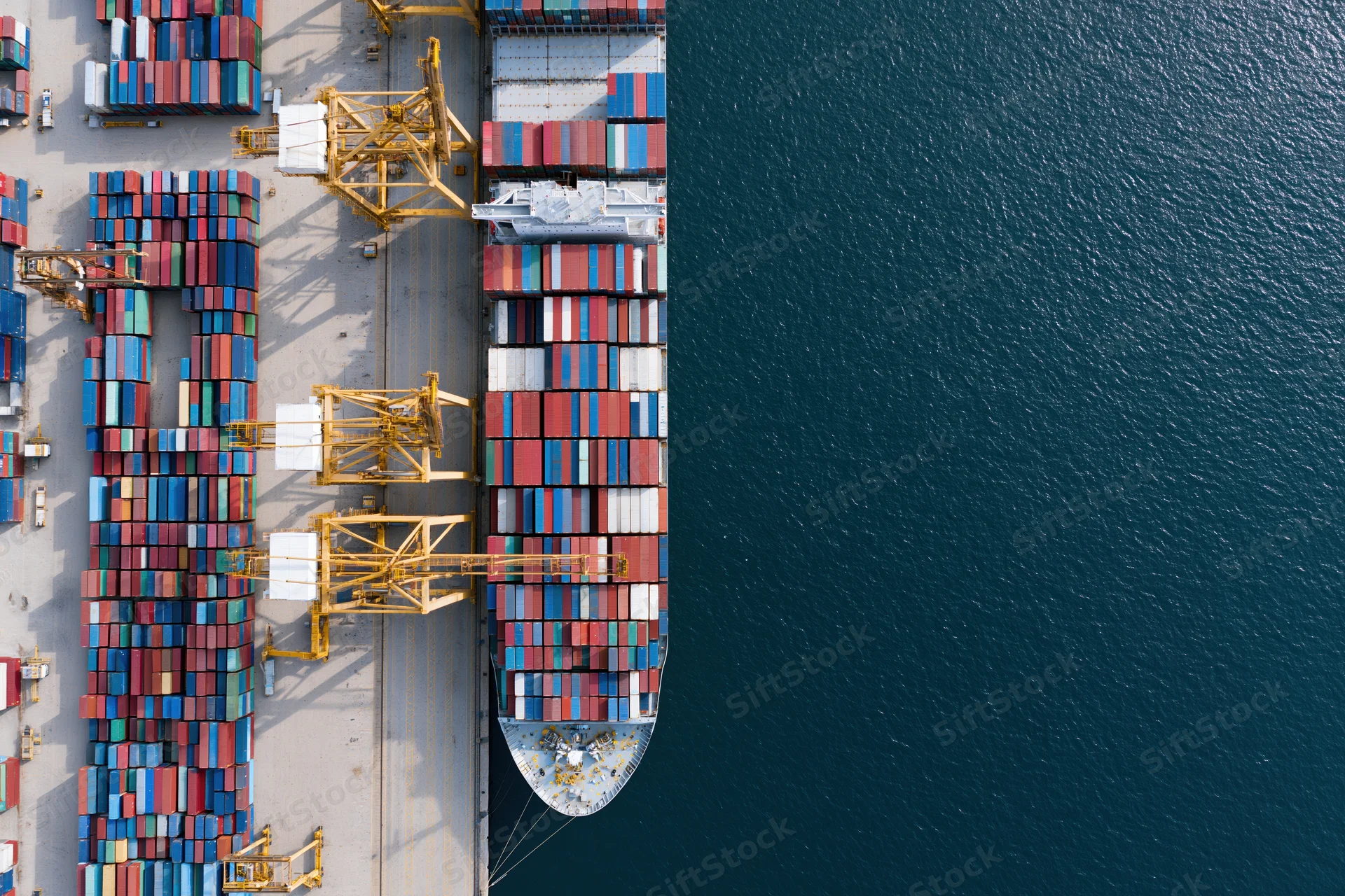 Aerial top-down view of a container ship docked at a busy commercial port with cranes and stacked cargo containers