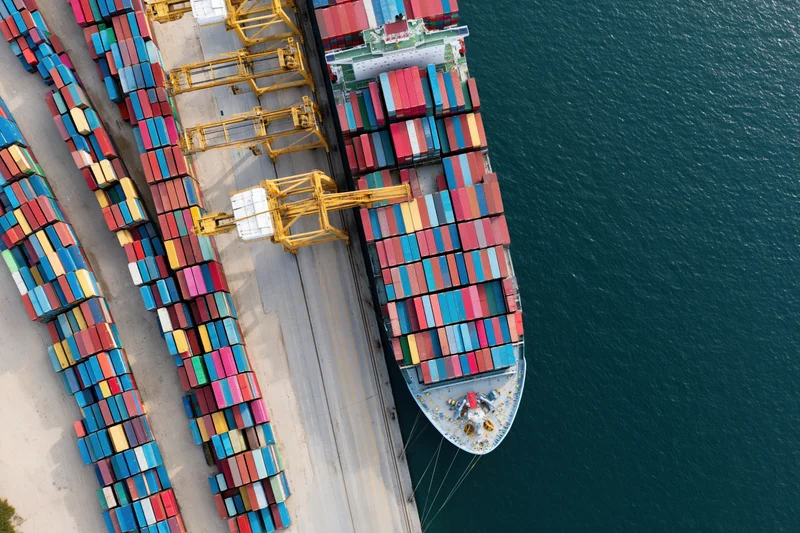 Container ship docked at port with cranes loading cargo from stacks on shore