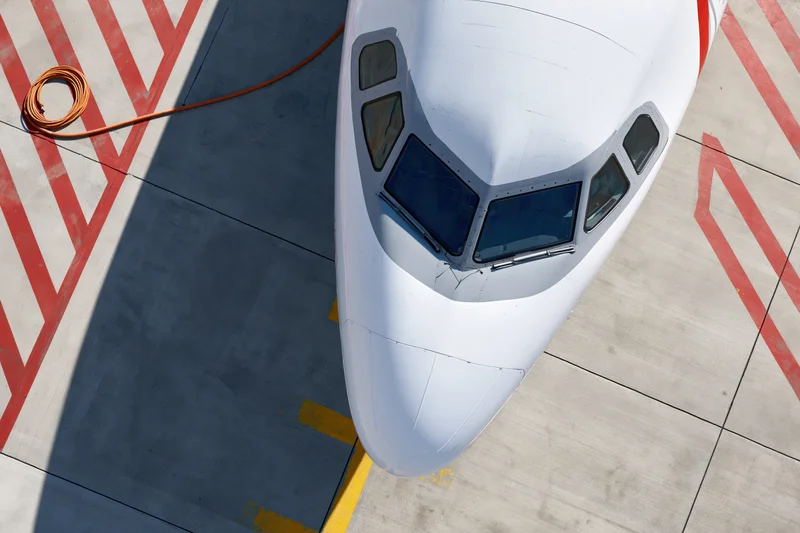 Top-down view of commercial airplane nose and cockpit on airport tarmac