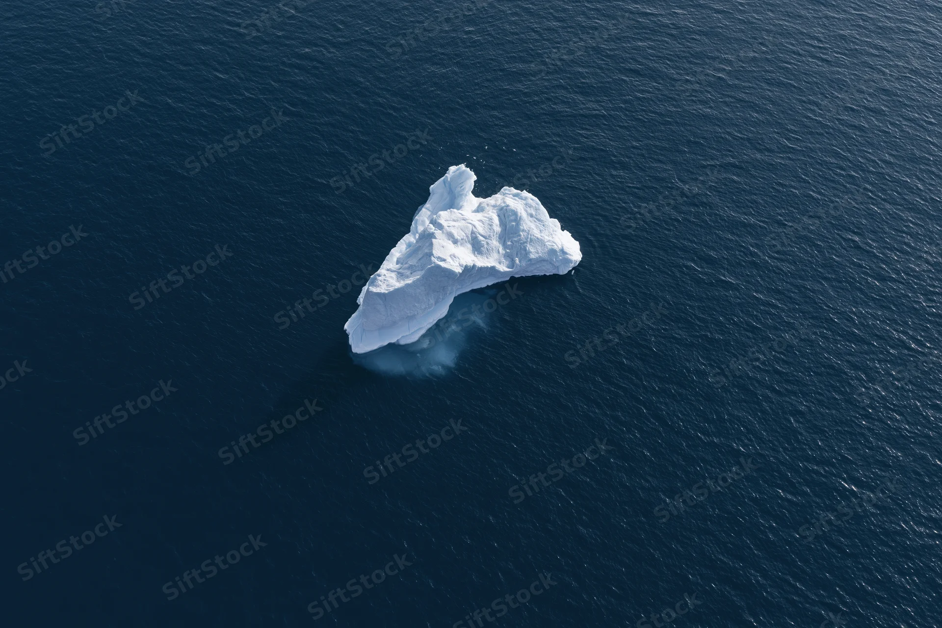 Aerial top-down view of a lone iceberg floating in deep polar ocean
