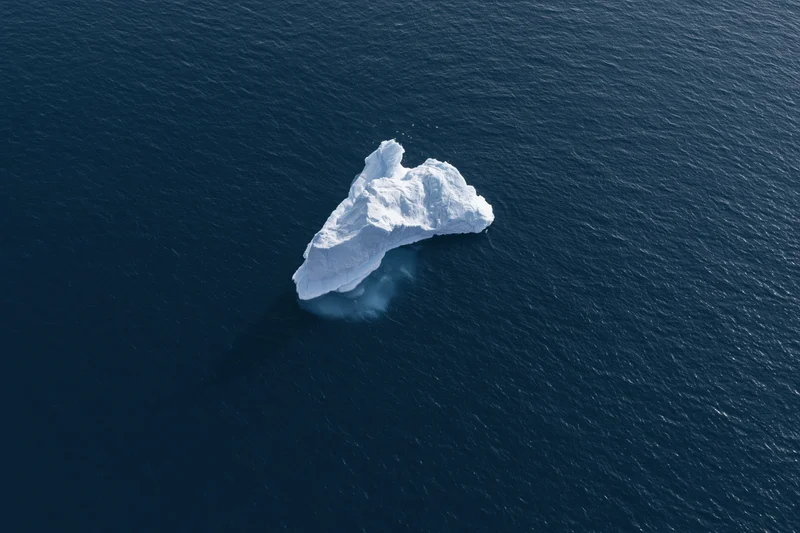Aerial top-down view of a lone iceberg floating in deep polar ocean