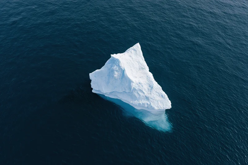 Aerial top-down view of a lone iceberg floating in deep polar ocean