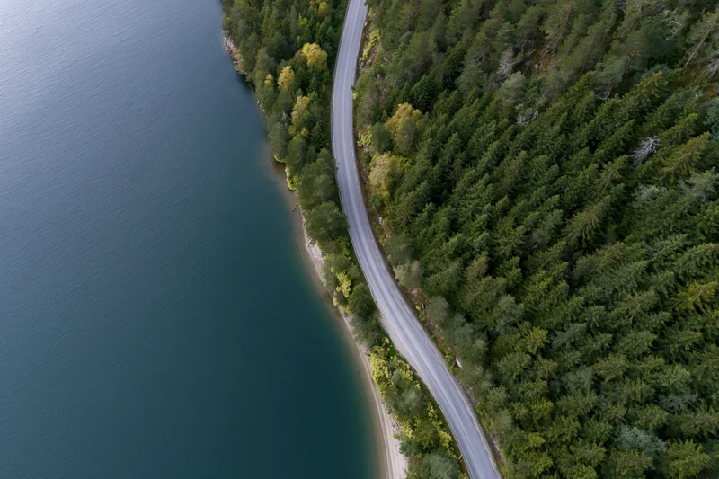 Aerial top-down view of a winding road curving along a forested shoreline beside a lake