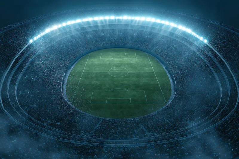Aerial top-down view of a packed soccer stadium at night with illuminated field and crowd