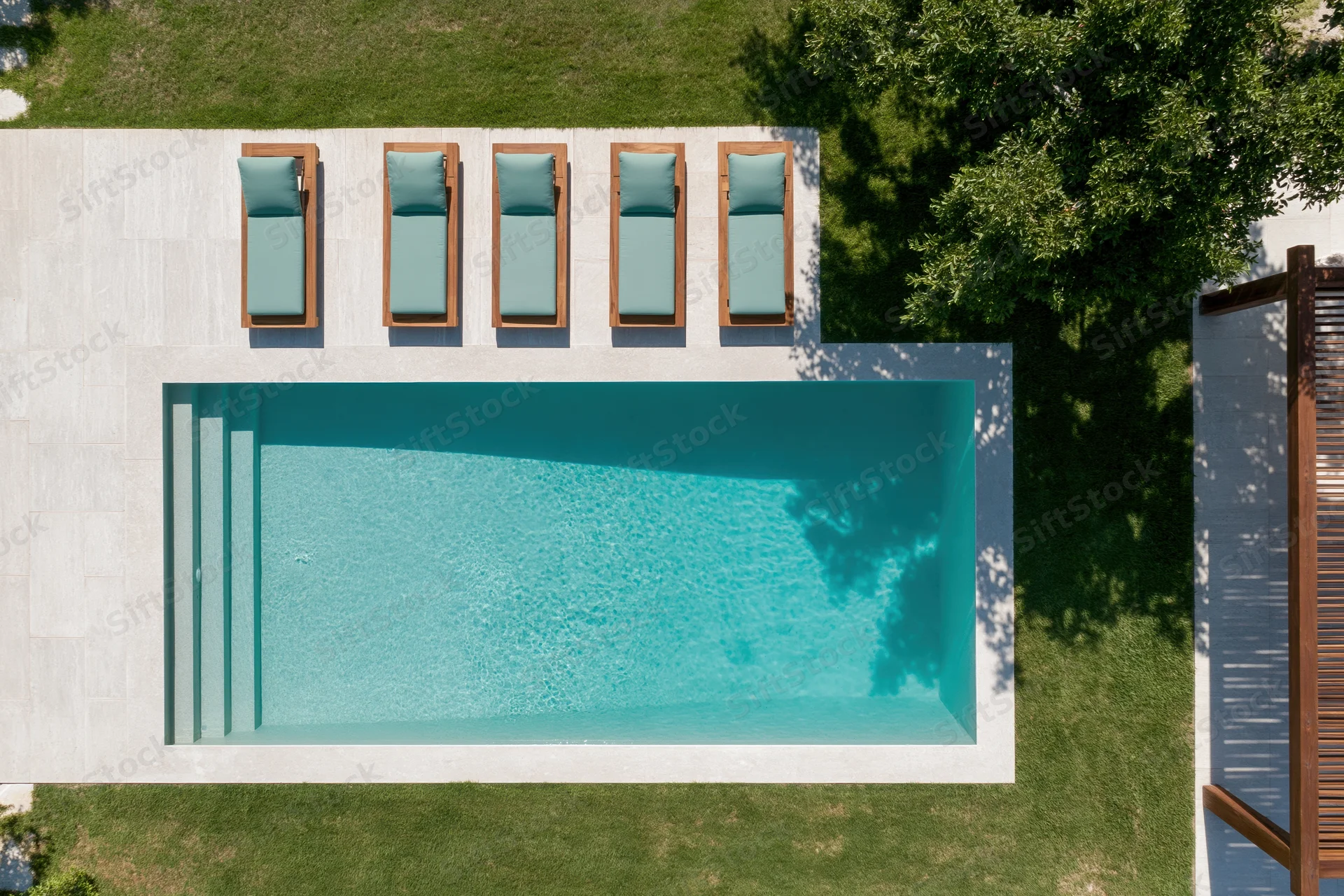 Aerial top-down view of a rectangular outdoor swimming pool with lounge chairs on a tiled deck surrounded by grass and trees