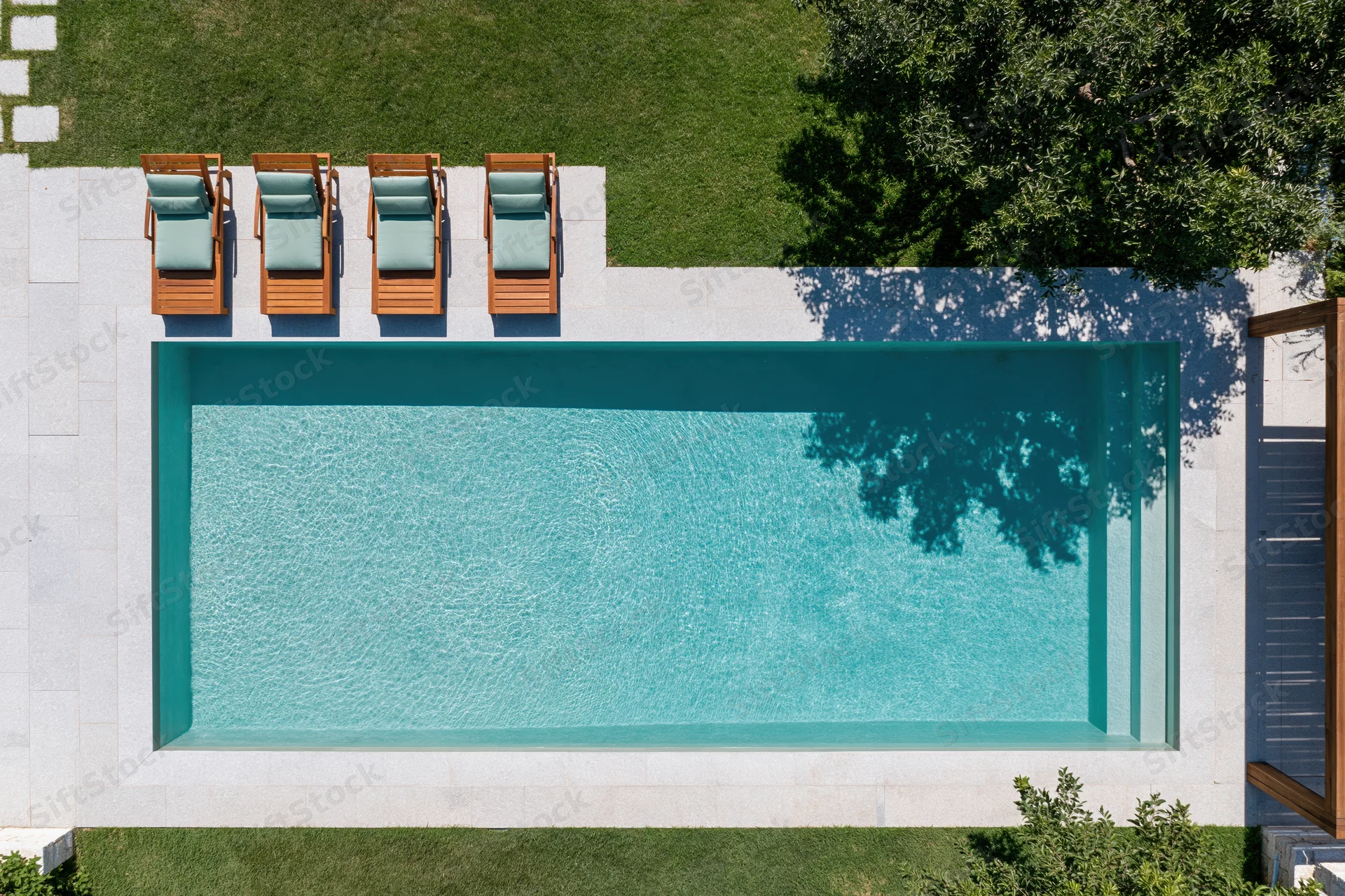 Aerial top-down view of a rectangular outdoor swimming pool with lounge chairs on a stone patio surrounded by green lawn
