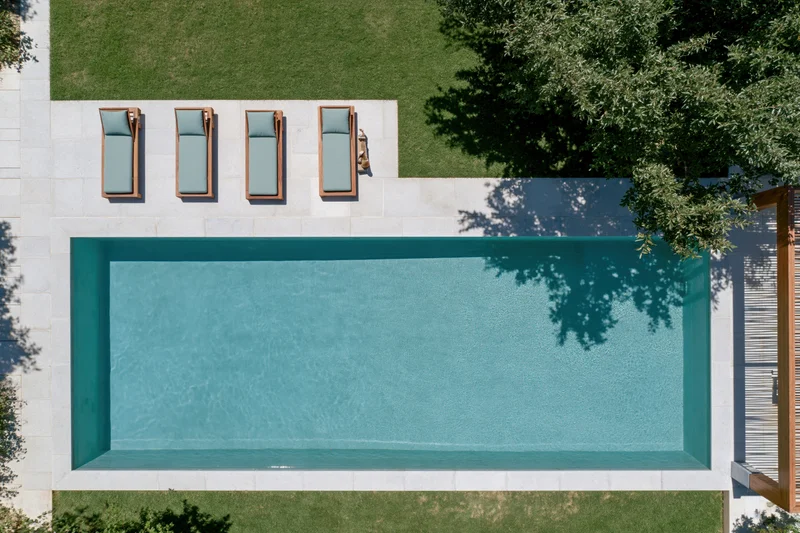 Aerial top-down view of a rectangular outdoor swimming pool with lounge chairs on a stone patio surrounded by grass and trees