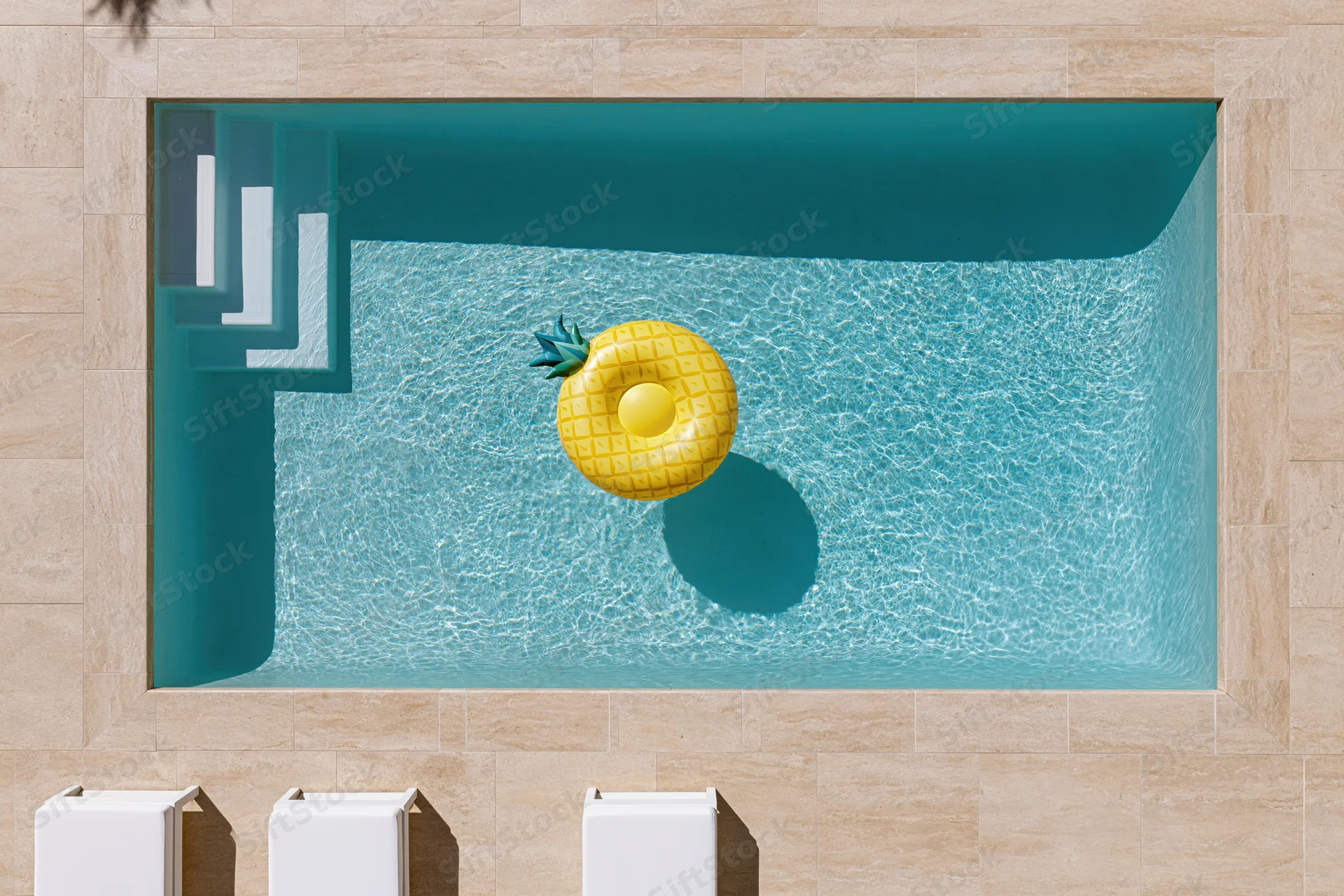 Aerial top-down view of a rectangular outdoor swimming pool with a yellow pineapple inflatable float and white steps, surrounded by beige stone tiles