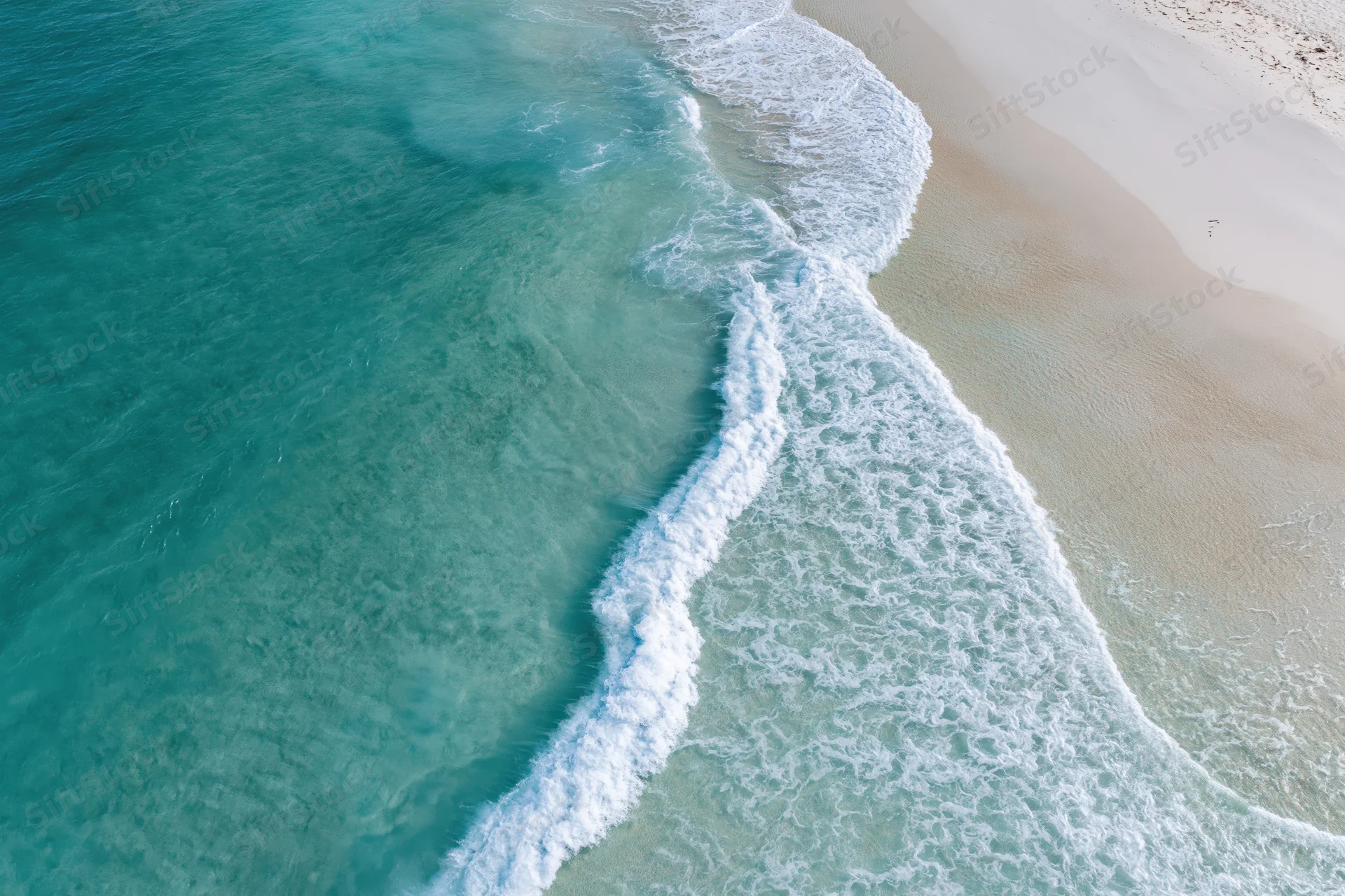 Aerial top-down view of turquoise ocean waves meeting white sandy beach