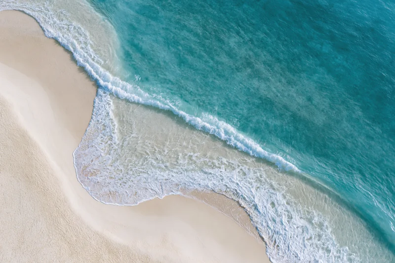 Aerial top-down view of turquoise ocean waves meeting white sandy beach