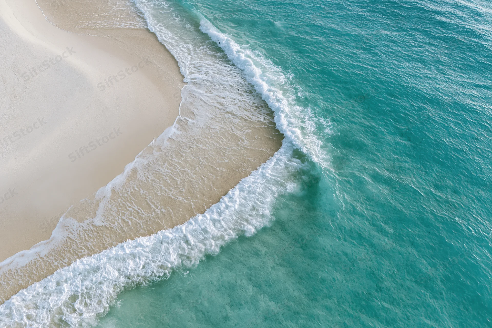 Aerial top-down view of turquoise ocean waves meeting white sand beach
