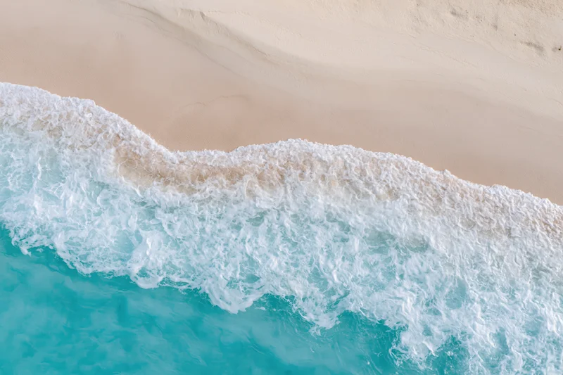 Aerial top-down view of turquoise ocean waves breaking on a sandy tropical beach