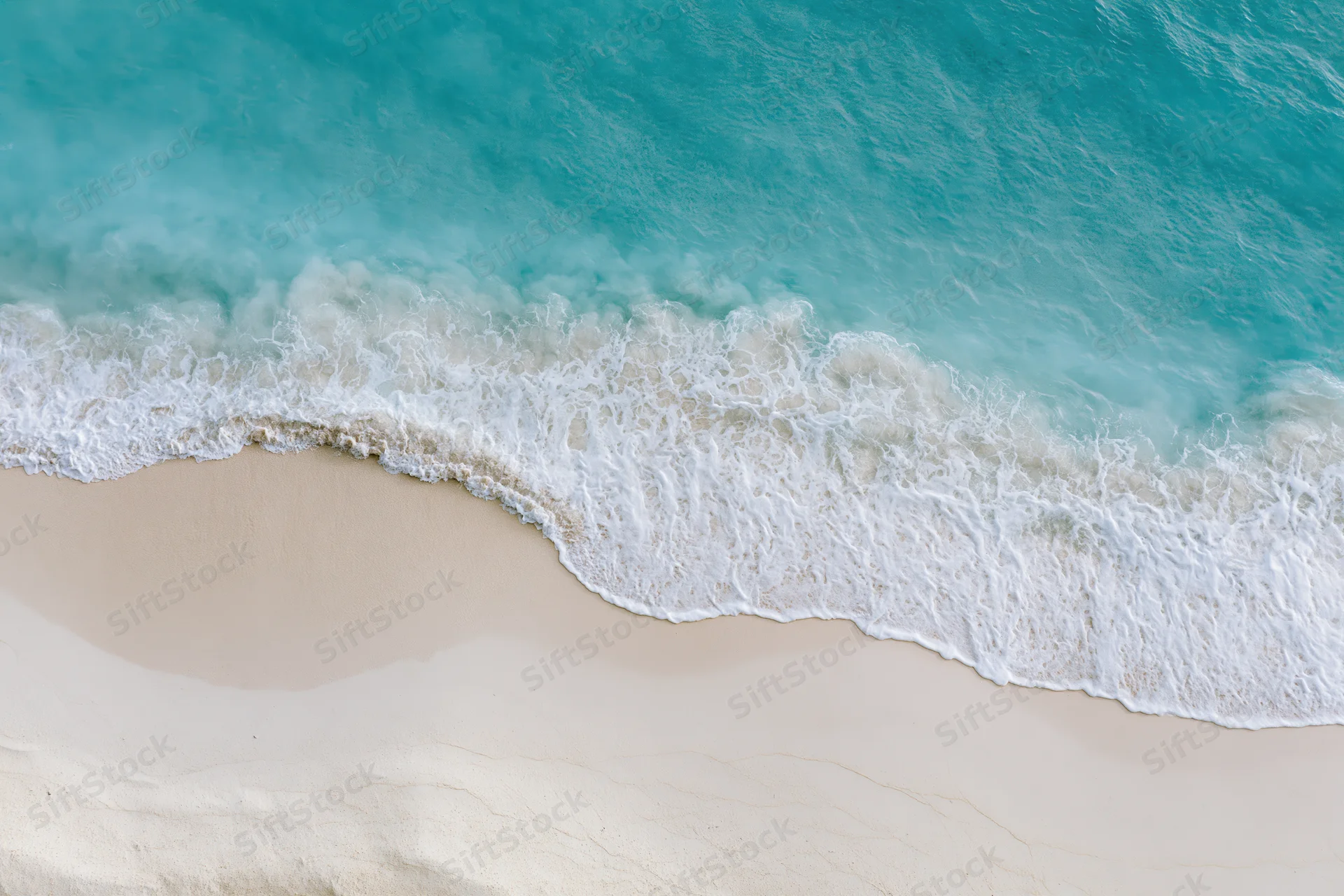Aerial top-down view of turquoise ocean waves meeting white sand beach
