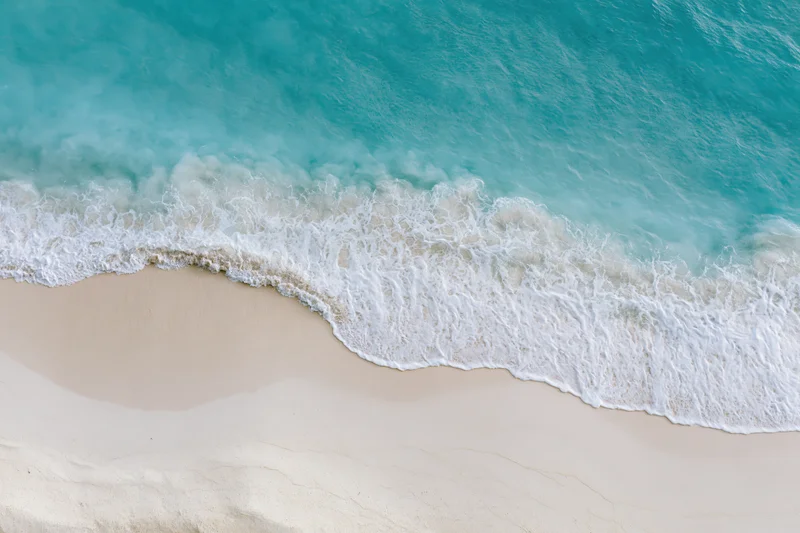 Aerial top-down view of turquoise ocean waves meeting white sand beach