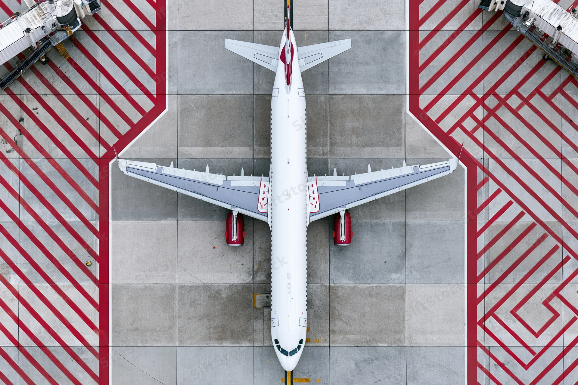 White commercial passenger jet parked on tarmac with red striped markings viewed from above
