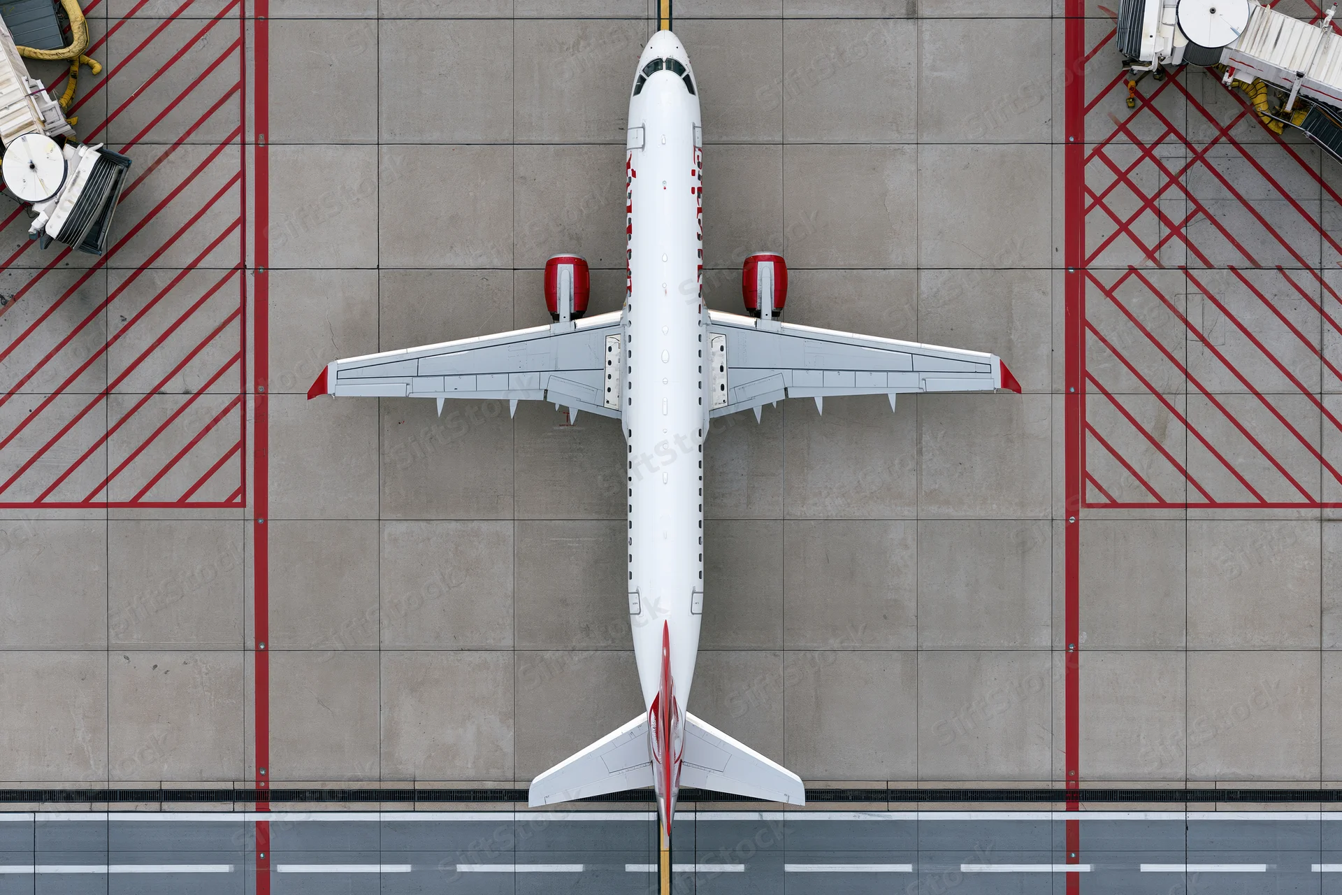 White commercial passenger jet viewed from above on airport tarmac with red ground markings