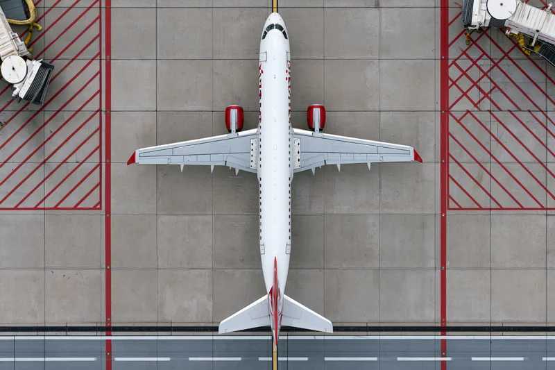 White commercial passenger jet viewed from above on airport tarmac with red ground markings