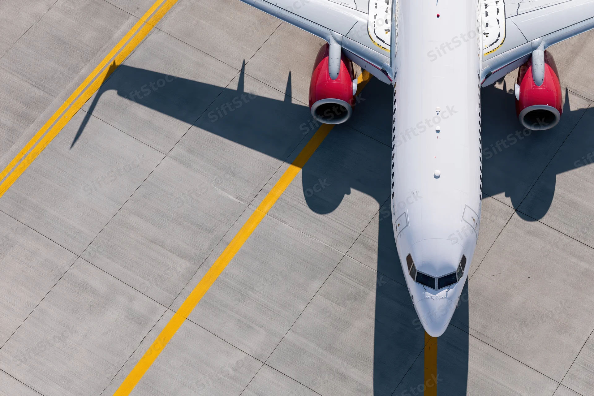 White commercial passenger jet taxiing on airport tarmac viewed from above