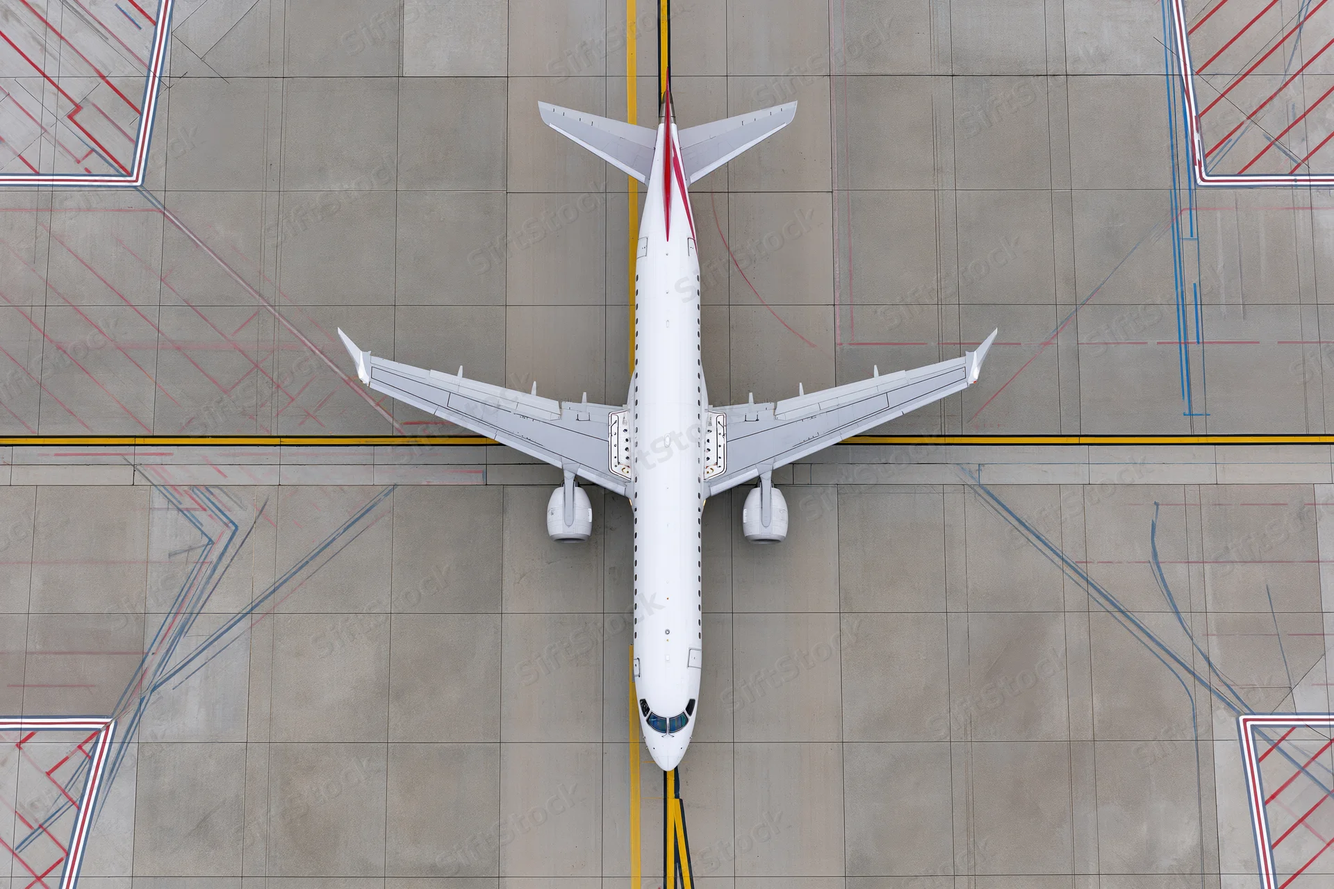 White commercial passenger jet viewed from above on airport tarmac with painted ground markings