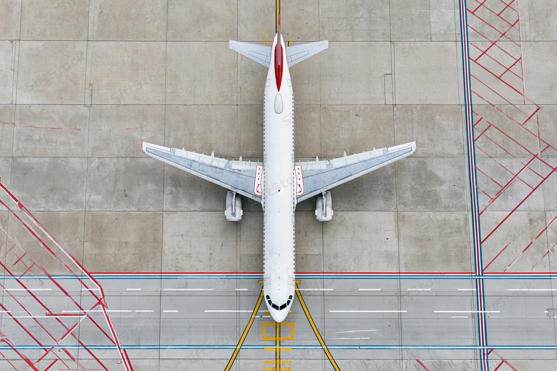 Overhead view of a white commercial passenger jet taxiing on airport tarmac with painted ground markings