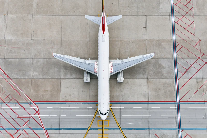 Overhead view of a white commercial passenger jet taxiing on airport tarmac with painted ground markings