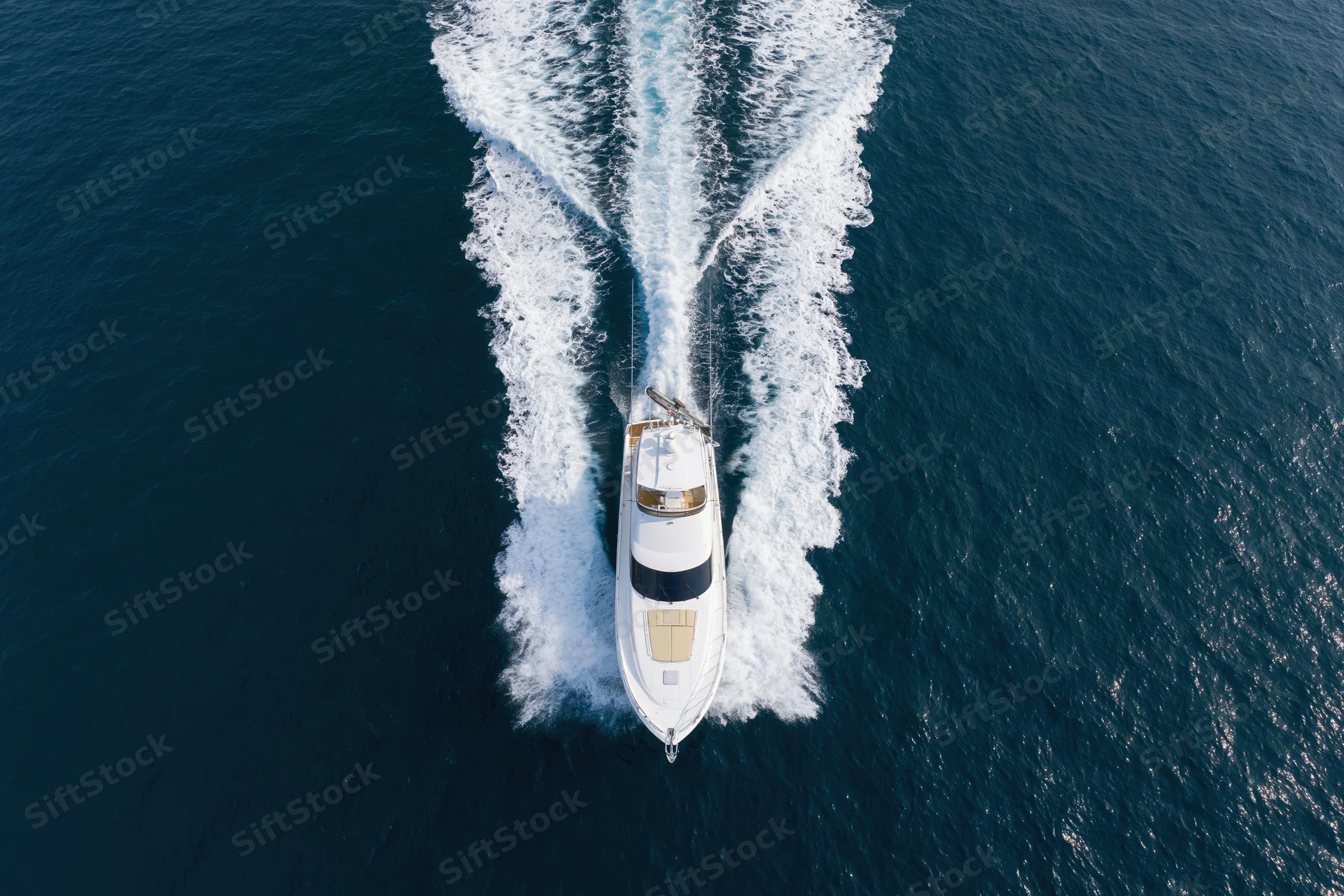 White motor yacht moving through deep blue ocean from aerial top-down view