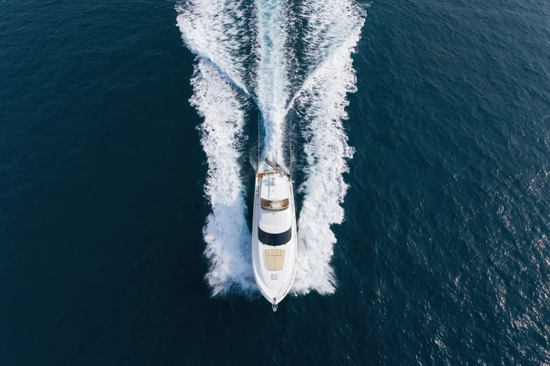 White motor yacht moving through deep blue ocean from aerial top-down view