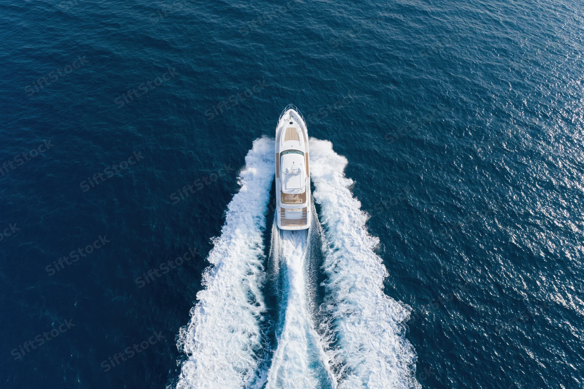 White motor yacht moving through deep blue ocean leaving a foamy wake from aerial top-down view