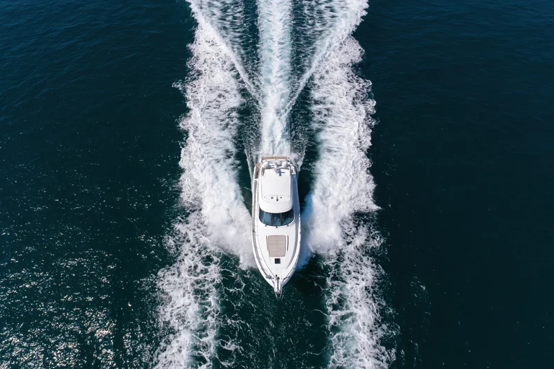 White motor yacht moving at speed across deep blue ocean, leaving a foamy wake behind