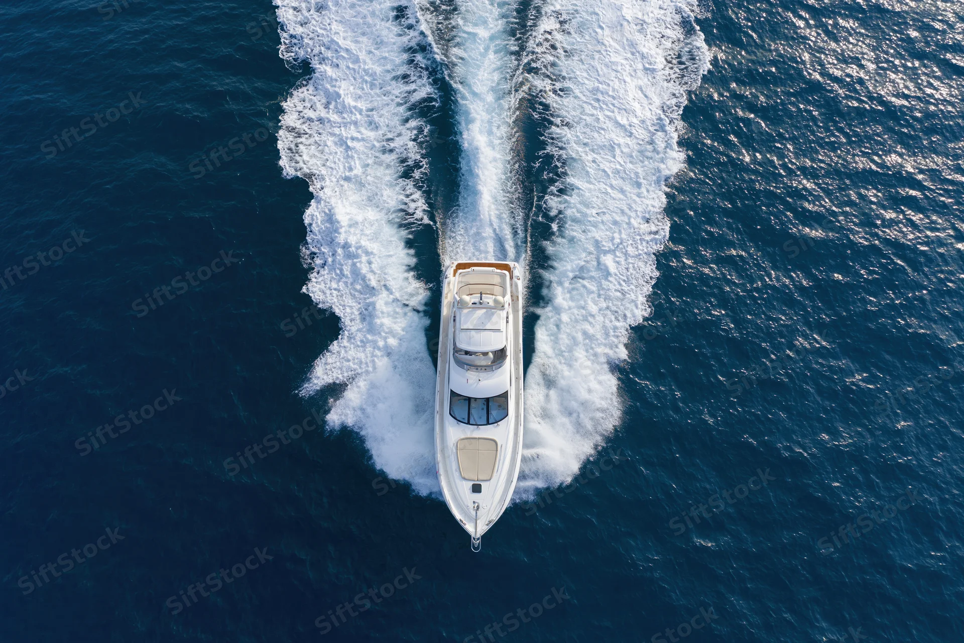 White motor yacht moving at speed across deep blue ocean, viewed from above, leaving a foamy wake behind