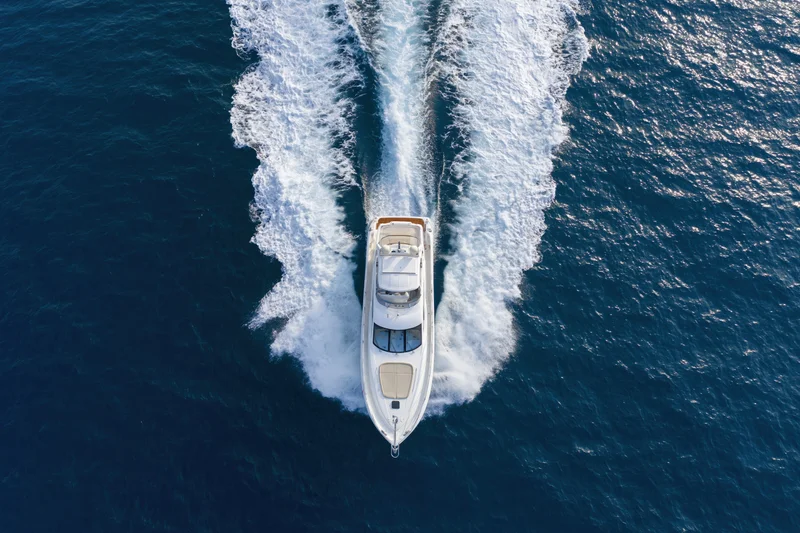 White motor yacht moving at speed across deep blue ocean, viewed from above, leaving a foamy wake behind