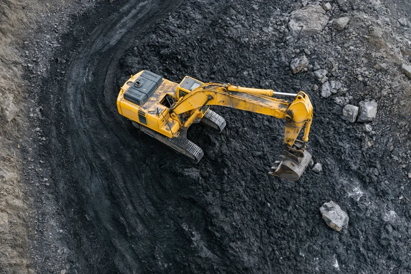 Yellow hydraulic excavator digging in open pit coal mine from aerial top-down view