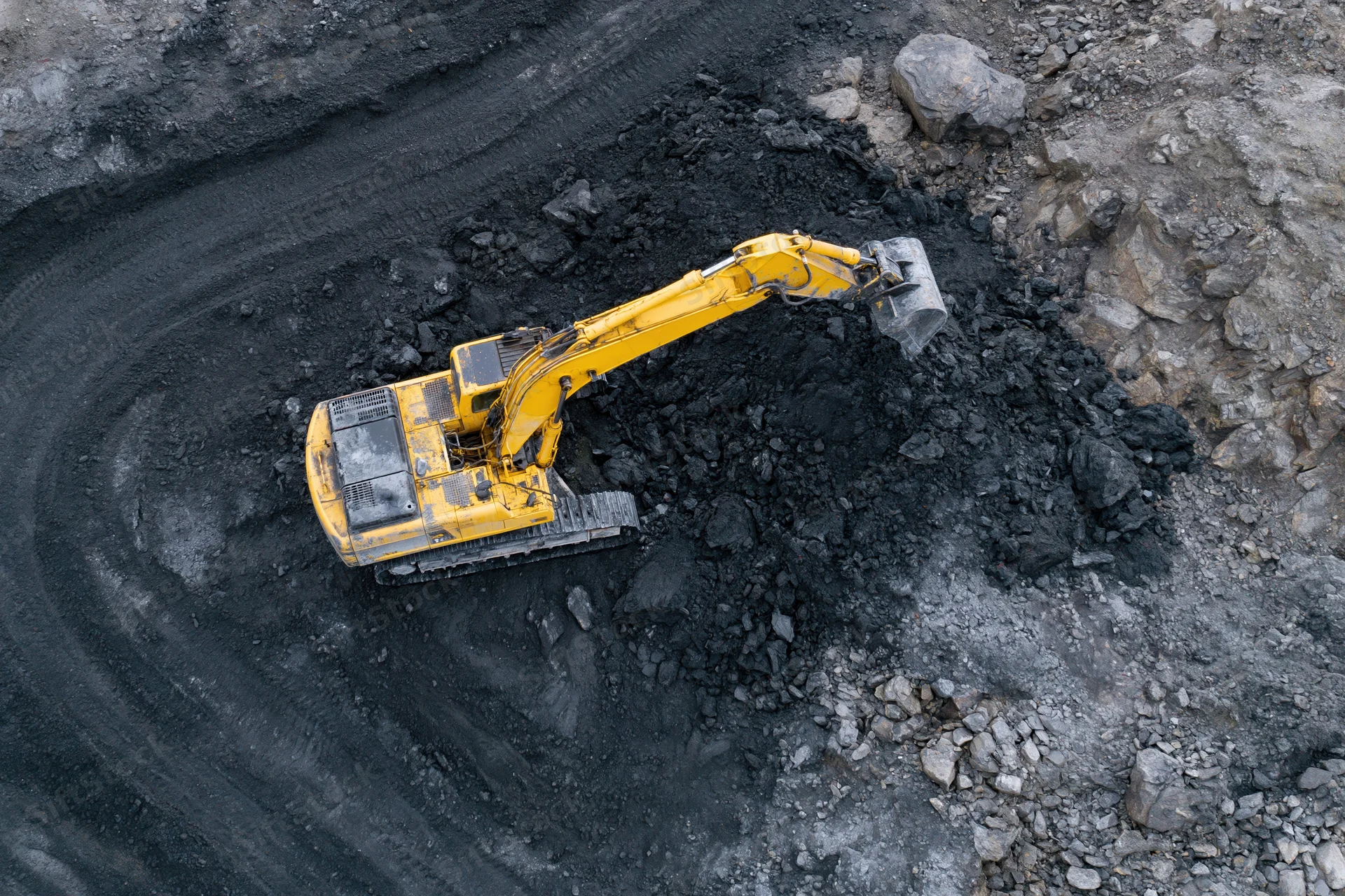 Yellow excavator digging coal in an open-pit mine from above