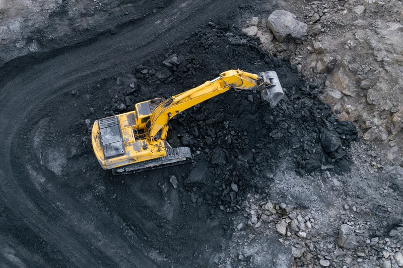 Yellow excavator digging coal in an open-pit mine from above