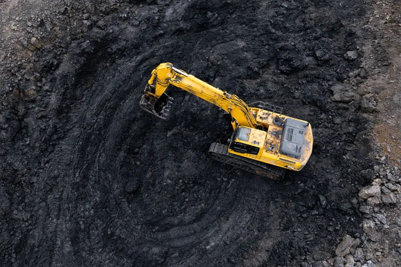 Yellow excavator digging in open-pit coal mine from above