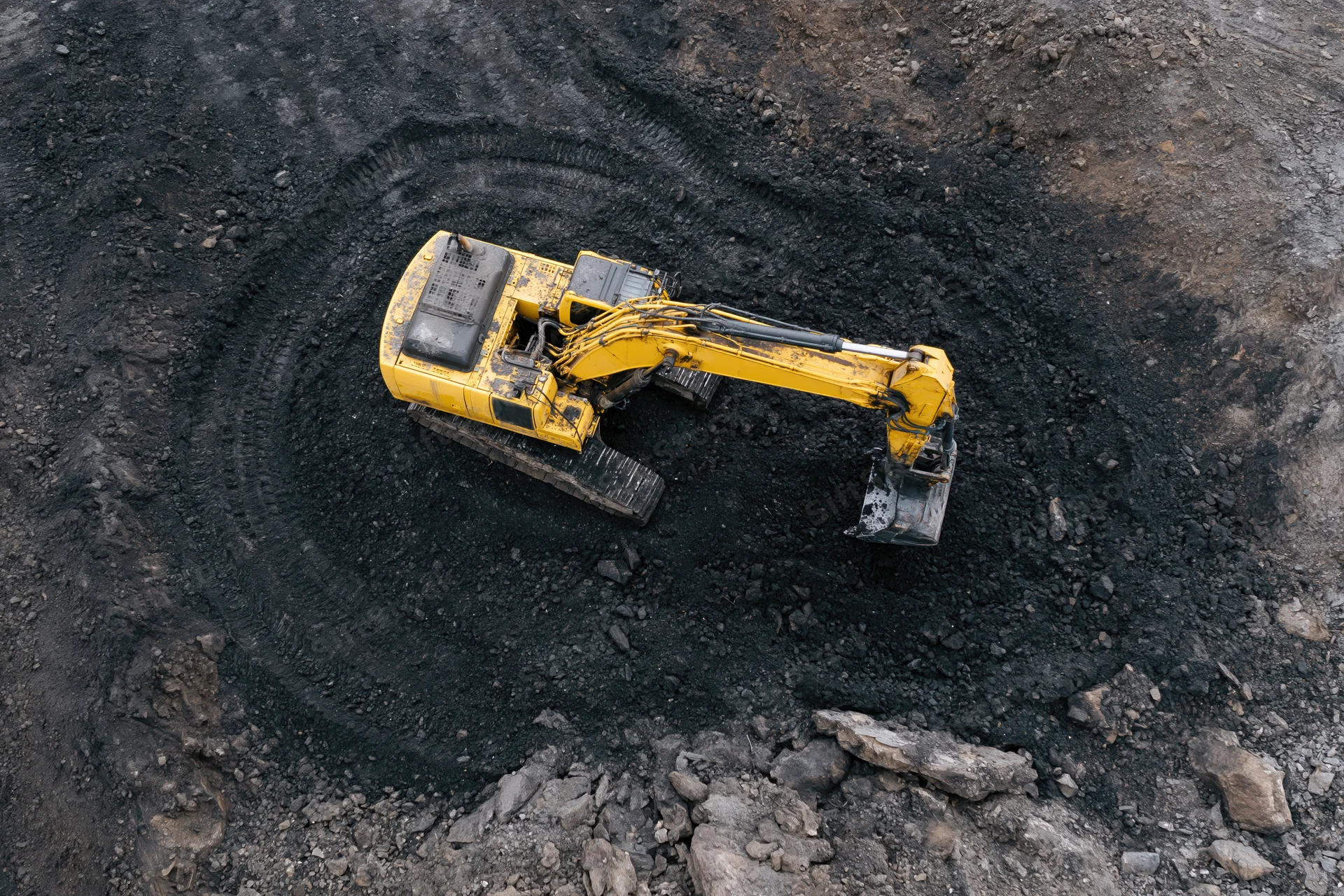 Yellow hydraulic excavator digging in a coal mine from above