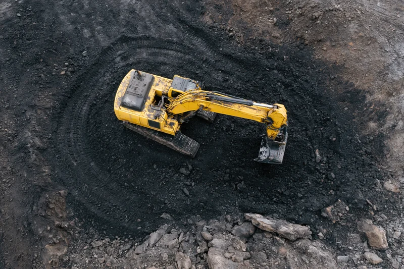 Yellow hydraulic excavator digging in a coal mine from above