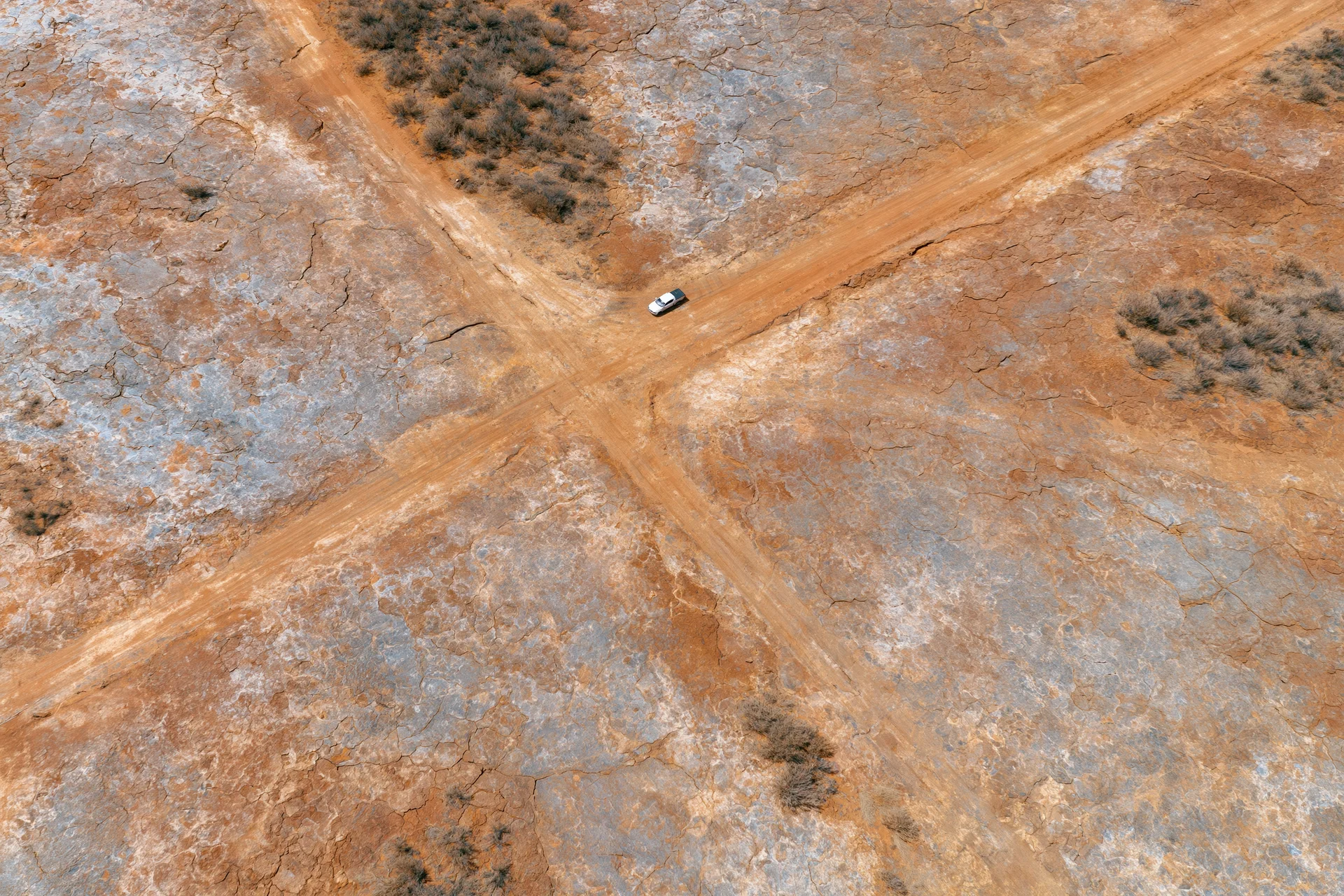 Aerial top-down view of a white car at a dirt road intersection in a cracked arid desert landscape
