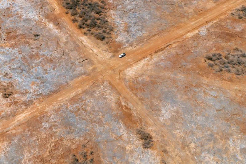 Aerial top-down view of a white car at a dirt road intersection in a cracked arid desert landscape