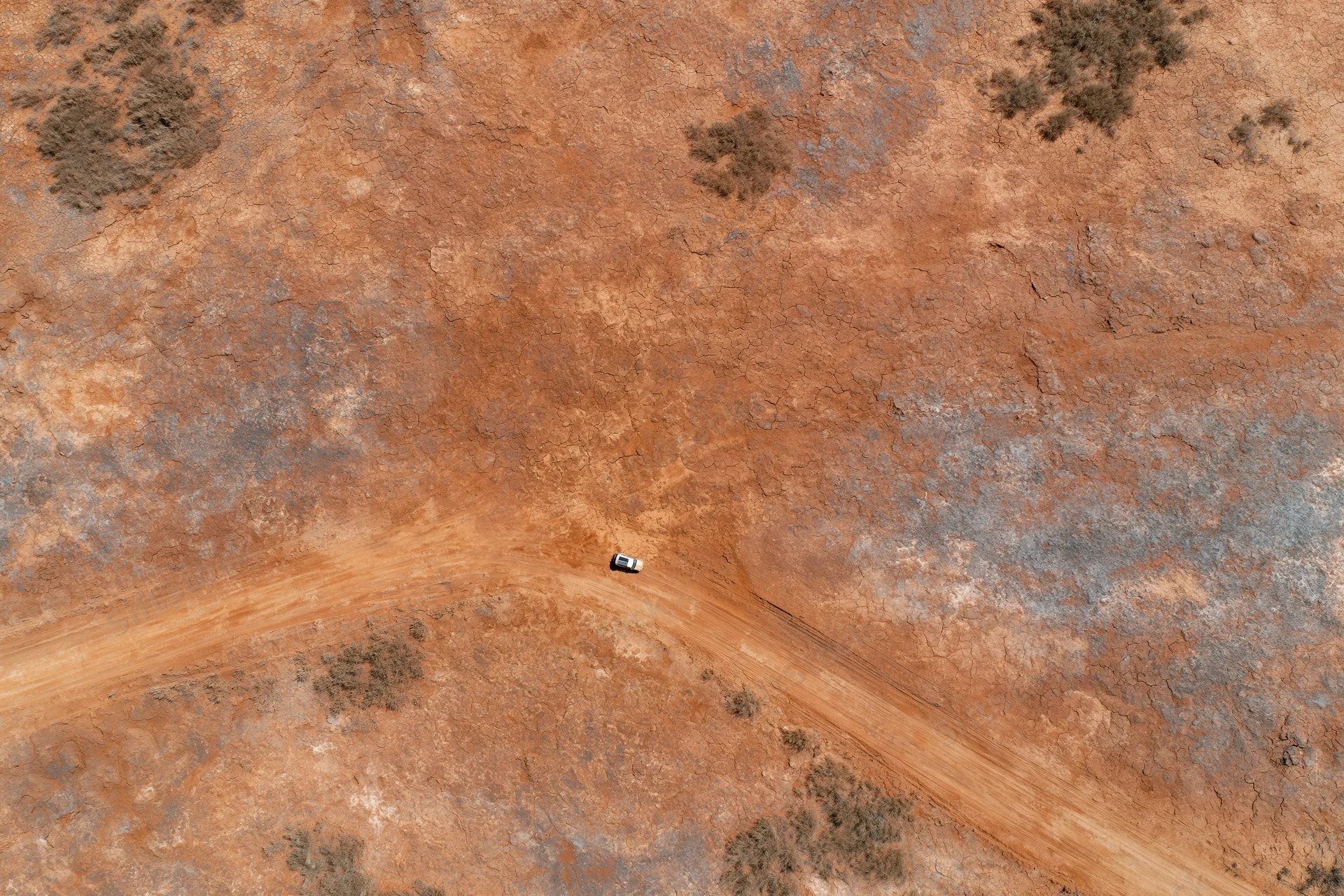 Aerial top-down view of a vehicle driving on a dirt road through an arid desert landscape
