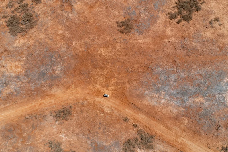 Aerial top-down view of a vehicle driving on a dirt road through an arid desert landscape