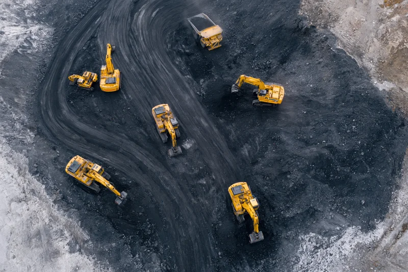 Aerial top-down view of yellow excavators and dump trucks operating in an open-pit coal mine