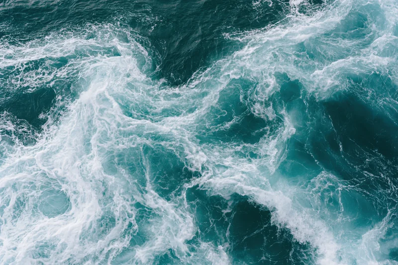 Aerial top-down view of churning deep ocean water with white foam and swirling currents