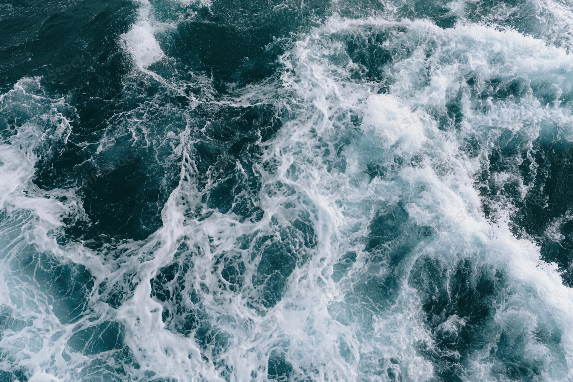 Aerial top-down view of churning deep ocean water with white foam