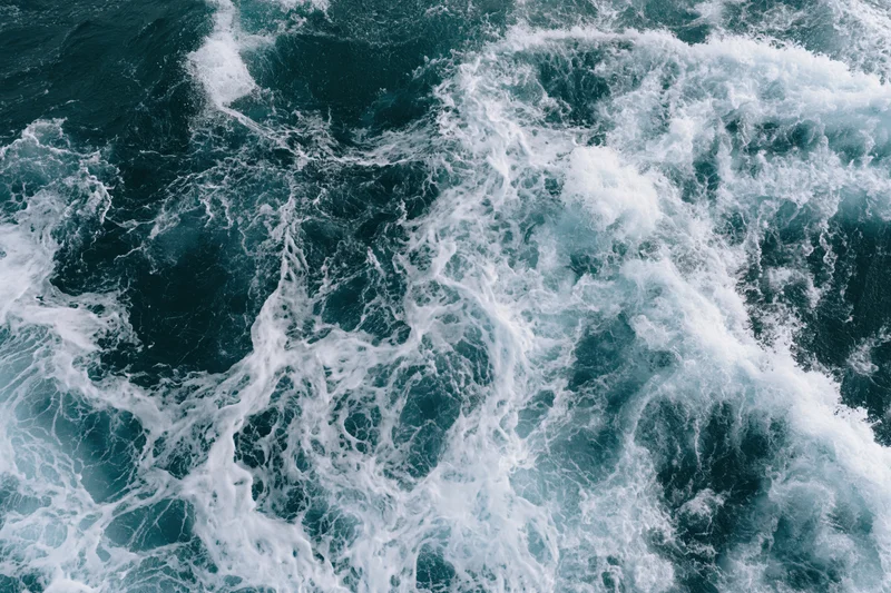 Aerial top-down view of churning deep ocean water with white foam