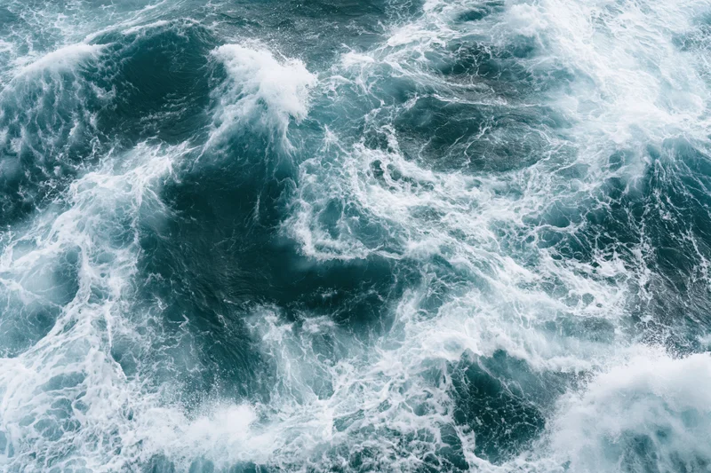 Top-down view of churning deep ocean waves with white foam and swirling currents