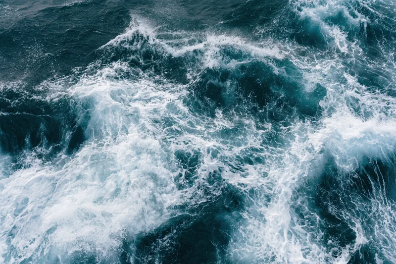 Aerial top-down view of churning deep ocean water with white foam