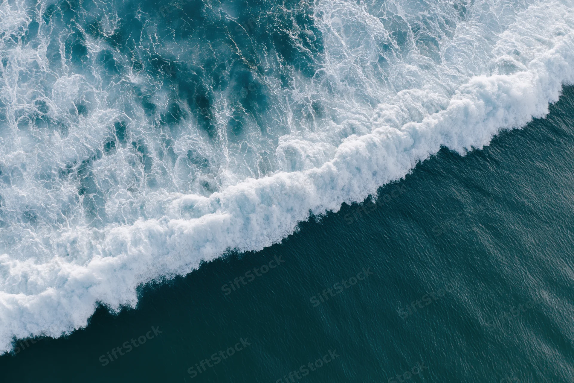 Aerial top-down view of ocean waves breaking in a diagonal line with white foam and deep blue water